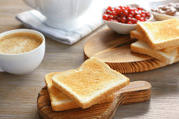 Wooden board with tasty breakfast toasts on table