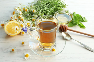 Glass cup with delicious chamomile tea on light wooden background