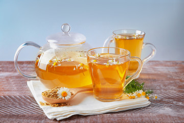 Glass teapot and cups with hot chamomile tea on table