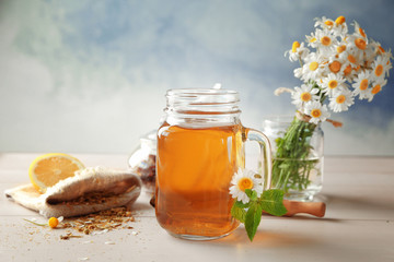 Composition with tasty chamomile tea in mason jar on light wooden table