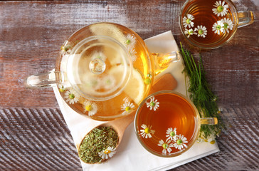 Glass teapot and cups with hot chamomile tea on table