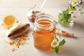 Mason jar with tasty chamomile tea on light wooden table