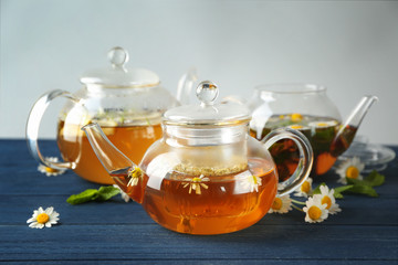 Composition with tasty chamomile tea in glass teapots on color wooden table