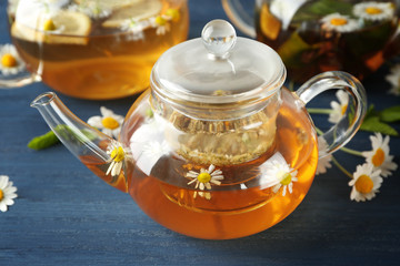 Glass teapot with hot chamomile tea on color wooden background
