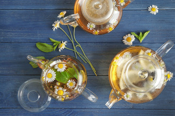 Composition with tasty chamomile tea in glass teapots on color wooden background