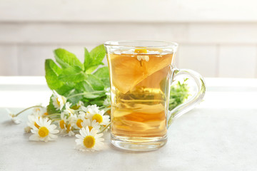 Herbal tea with lemon in glass cup and chamomile flowers on table