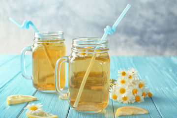 Composition with tasty chamomile tea in mason jars on color wooden table