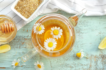 Glass teapot with tasty chamomile tea on color wooden background