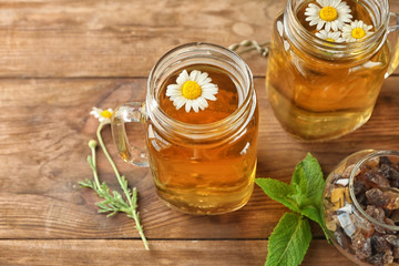Mason jars with chamomile tea on wooden background
