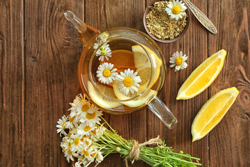 Composition with chamomile tea in glass teapot on wooden background