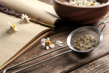 Strainer with dried milled chamomile on wooden background