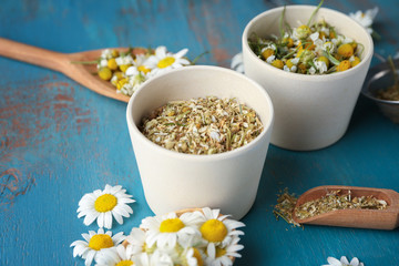 Bowls with dried chamomile flowers on color wooden background