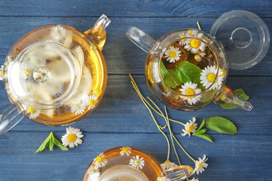 Composition with tasty chamomile tea in glass teapots on color wooden background