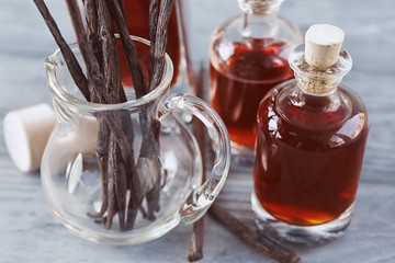 Bottles with aromatic extract and dry vanilla beans in jug on table