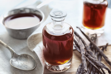 Bottle with aromatic extract and dry vanilla beans on table