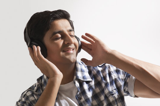Relaxed young guy listening music over colored background 