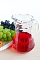A jug of grape juice, fruit on a white plate