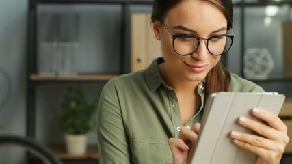 Young business woman in glasses using tablet computer touchscreen in the modern urban office and smiling. close up - Powered by Adobe