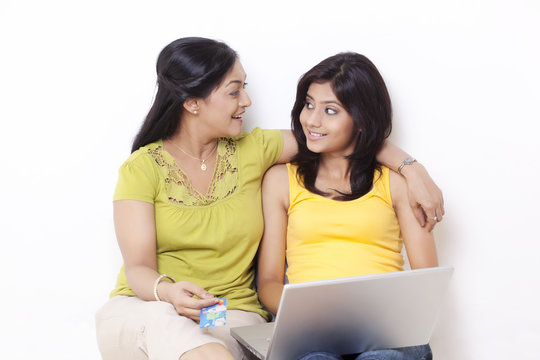 Mid adult woman and her daughter looking at each other while shopping online 