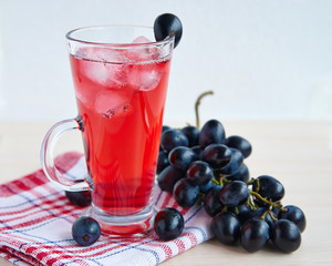 A glass of juice with ice and a brush of black grapes