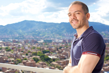 Man on a balcony looking side view, staring at the mountain city horizon