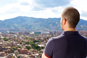 Fototapeta na wymiar Man from behind on a balcony staring at the mountain city horizon, focus on man