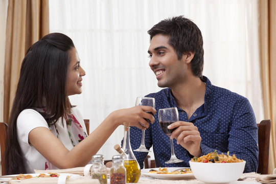 Happy young couple clinking wine glass while looking at each other at restaurant 