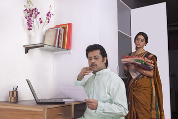 Man working on laptop and woman keeping clothes in cupboard