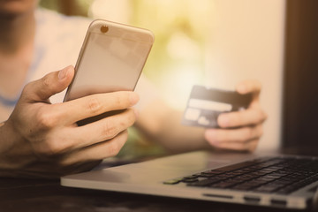 Close up young hipster hoding smart phone and credit card on wooden desk in coffee shop. Online payment and shopping online concept.