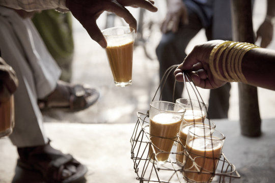 Male hand taking a glass of chai from tray held by woman 