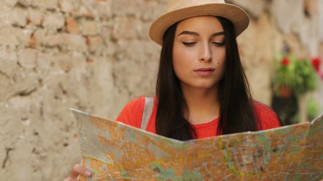 Young attractive woman searching interesting places and streets in travel paper map and smiling at the camera. Portrait shot