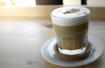 Glass of hot coffee drink in white plate on wooden table with lens flare.
