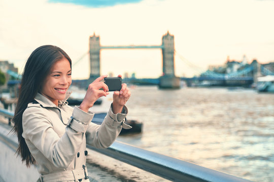 London woman tourist taking photo of Tower Bridge with mobile smart phone camera. Girl enjoying view over the River Thames, London, England, Great Britain. United Kingdom tourism concept.