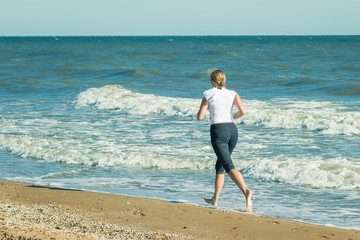 Fototapeta na wymiar A woman in a white sports jacket is Jogging on the beach.