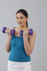 Fototapeta na wymiar Portrait of young woman lifting dumbbells against gray background 