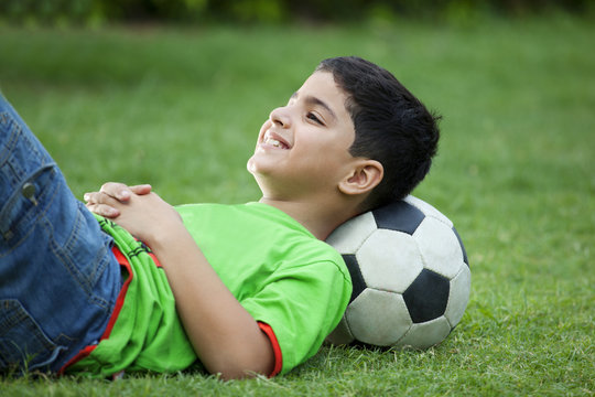 Smiling boy lying on grass with soccer ball 