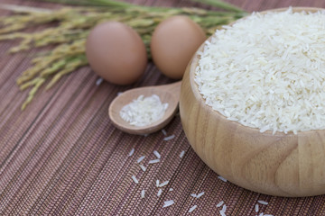 Close up Jasmine Rice on wooden bowl, Next to chick eggs and golden rice plant. Thai rice exported worldwide and famous. Blur background with Texture.