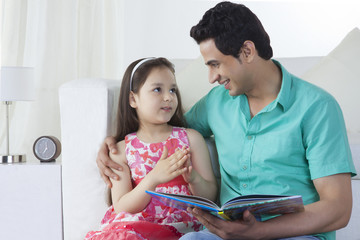 Little girl explaining story to father on sofa at home