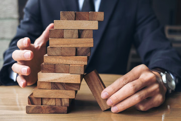 Alternative risk concept, plan and strategy in business, Young intelligent businessman raise the wood game, hands of executive sustain wood block on the tower, Collaborative management