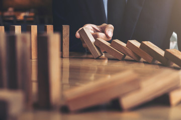 Close up of businessman hand Stopping Falling wooden Dominoes effect from continuous toppled or...