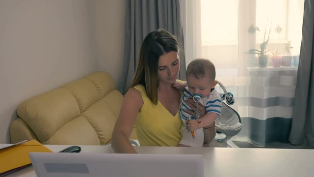 Young mother holds a baby in arms and working with laptop