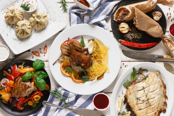 Dinner table with georgian cuisine. Grilled fish, khinkali, meat with caramelized apple, shawarma and other dishes with souce