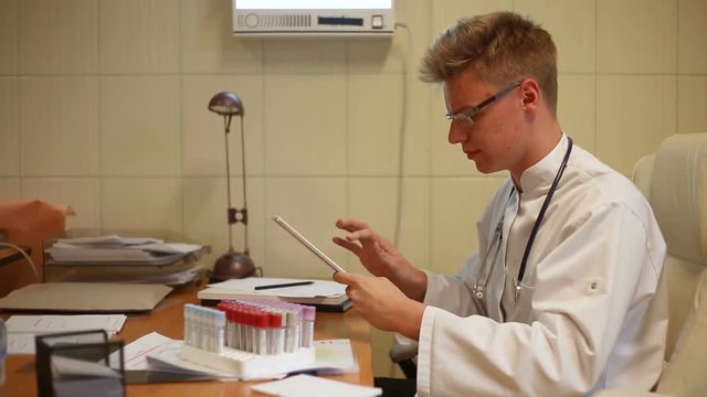 Doctor using tablet while sitting in the office and working on samples
