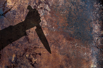 Human hand with big killing knife silhouette in shadow on rust wall background. Illustration for criminal news.