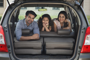 Portrait of young family leaning on back seat with open boot of car	