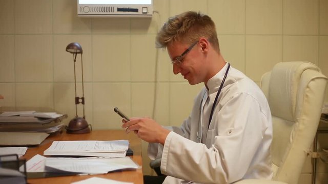 Doctor sitting in the office and texting messages on smartphone
