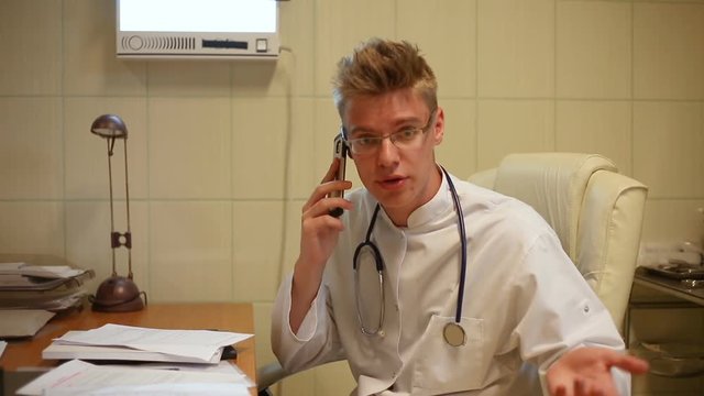 Doctor having problems with papers and looks angry while speaking on cellphone
