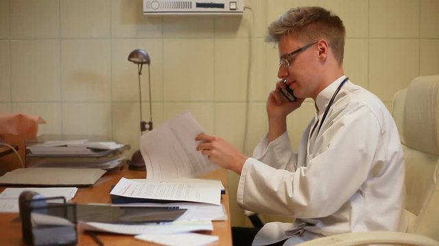 Doctor looks worried while sitting in the office and talking on cellphone
