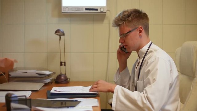 Doctor looks worried while speaking on cellphone and checking documents
