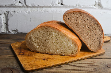 A loaf of bread on a wooden board against a white brick wall.